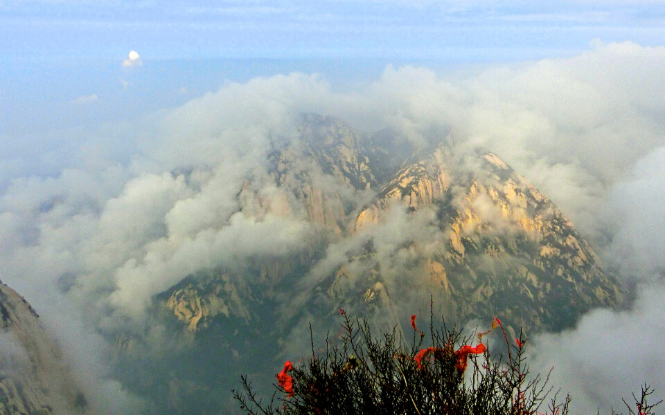 A photograph of mountain peaks in the clouds as seen from the top of a separate peak in China.